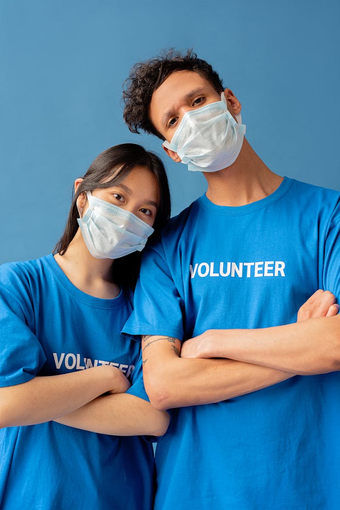Asian woman and black man volunteers posing in blue shirts with face masks.